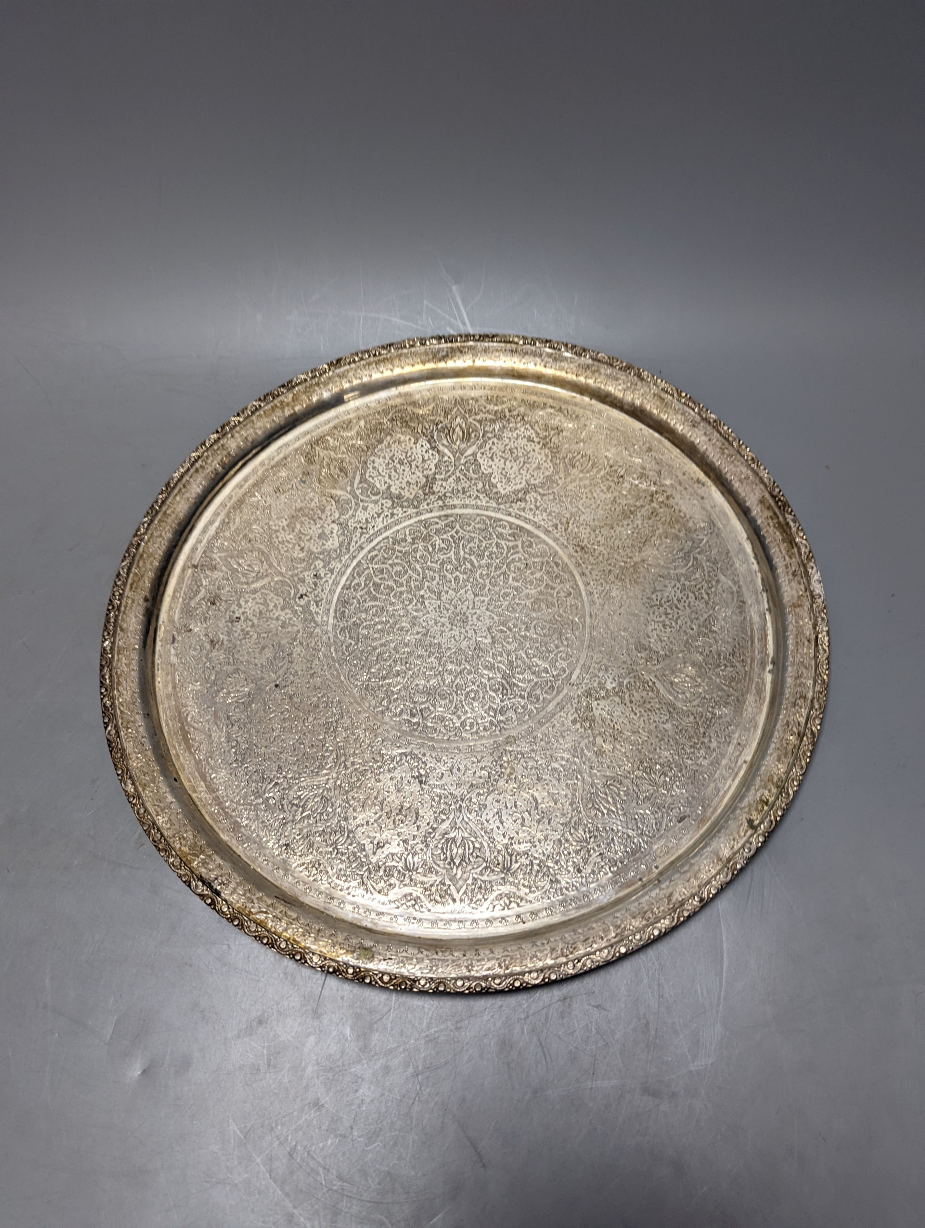 A Persian engraved white metal circular drink's tray by Vartan, 32cm, 747 grams and a white metal wall plaque.